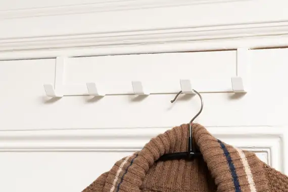 A Yamazaki home hanger hangs above the door with one sweater hanging from it.