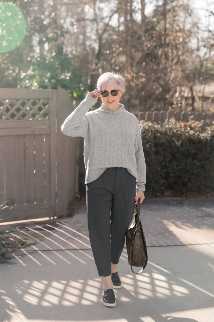 Classic style over 50 outfit with a gray cable knit sweater, charcoal tailored pants, and black loafers.