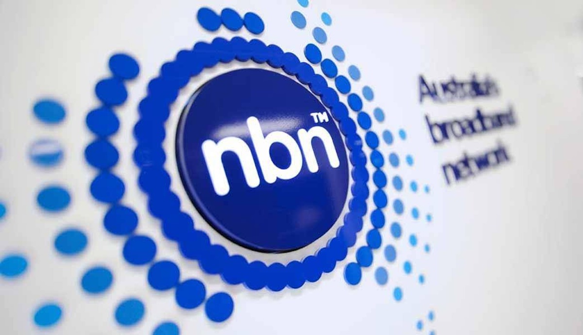 Dark blue NBN Co logo on a white wall blurred in the background