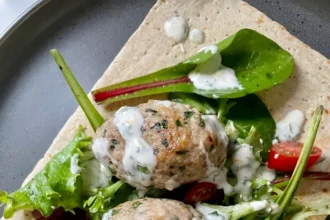 Overhead view of chicken kofta wrap with mixed greens, grape tomatoes, and yogurt sauce on lavash flatbread on a gray plate