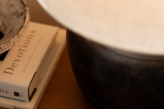 A marble tray holding several gold rings and earrings sits on a wooden surface next to a black pot and a stack of books, including one titled "Devotions.