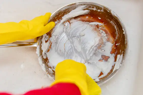 A man wearing rubber gloves soaps a grease-stained pan with baking soda.