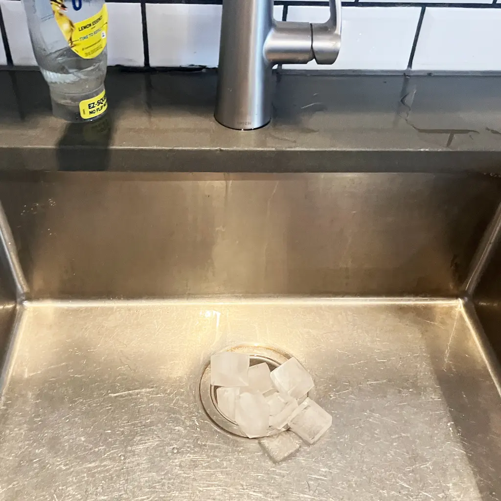 Stainless steel sink with ice cubes in garbage disposal.