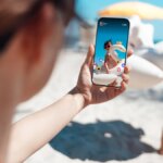 A person takes a social media  photo of family playing at the beach.
