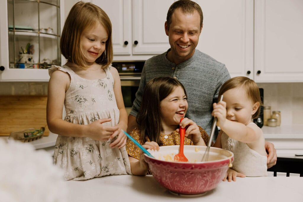 dad helps his kids bake cookies in a mixing bowl at home