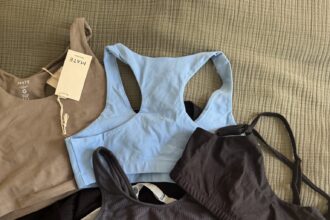 Several sports bras and bralettes in various colors, including blue, black, brown, and beige, are laid out on a textured fabric surface, some with tags attached.