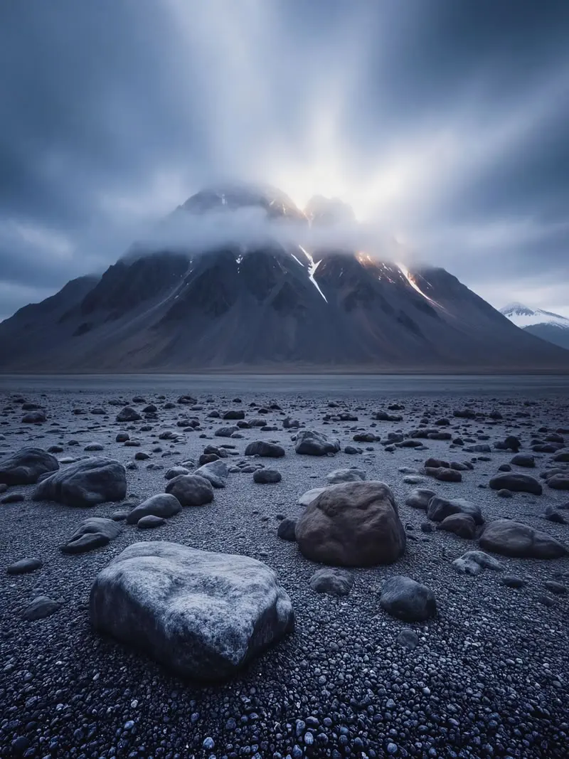 Dramatic sun rays breaking through clouds over rugged mountains and rocky volcanic beach in South Georgia, photographed by wildlife and nature photographer Christian Hartmann in the Southern Ocean wilderness.