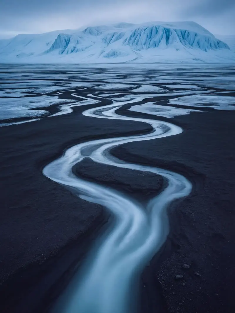 Winding glacial meltwater streams flowing across dark volcanic plains toward icy mountains in South Georgia, photographed by nature and wildlife photographer Christian Hartmann in the Southern Ocean polar wilderness.