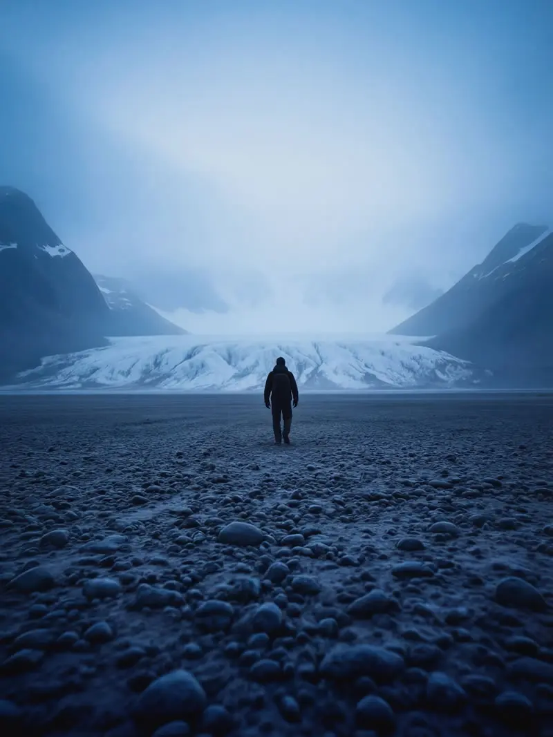Lone person walking across rocky beach toward massive glacier and mountains in South Georgia, photographed by nature and wildlife photographer Christian Hartmann in the Southern Ocean polar landscape.