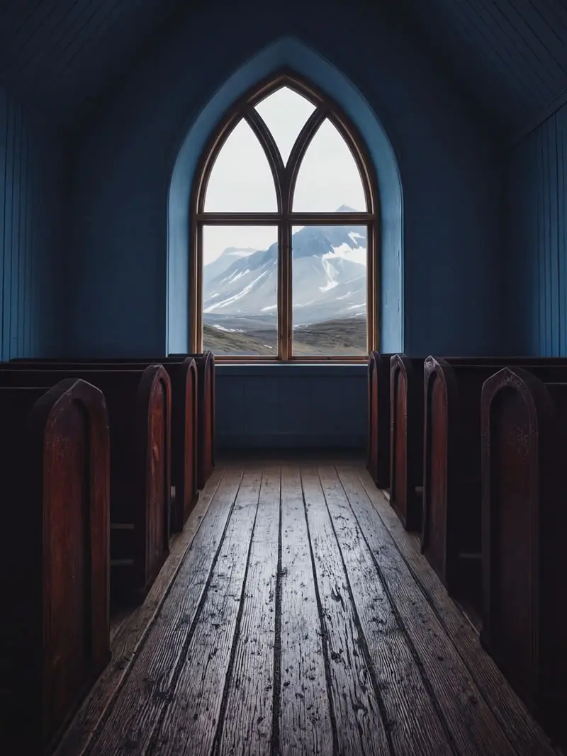 Interior of small wooden chapel with pews and arched window overlooking snowy mountains in South Georgia, photographed by nature photographer Christian Hartmann showing remote polar landscape through church window.
