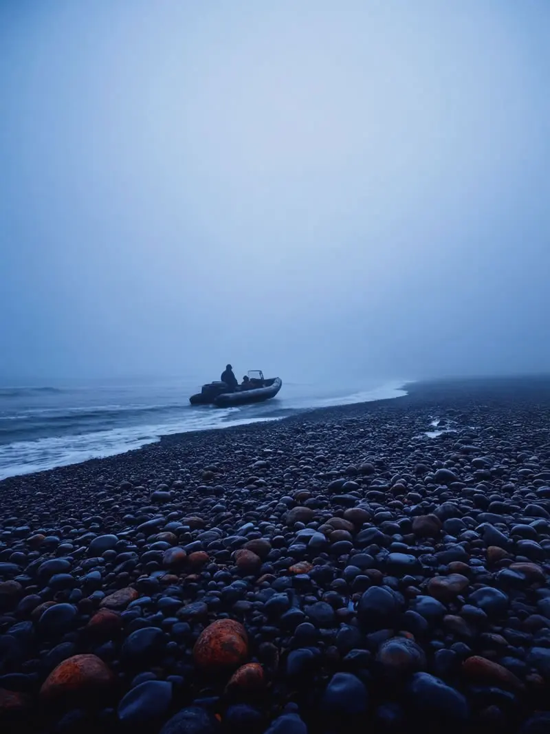 Expedition boat approaching foggy pebble beach in South Georgia with dark ocean and misty polar landscape, photographed by nature and wildlife photographer Christian Hartmann in the Southern Ocean wilderness.