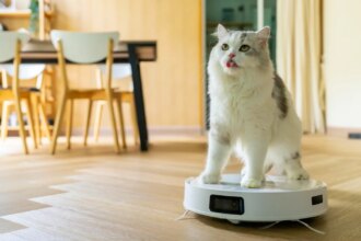 A cat on a robot vacuum in a dining room.